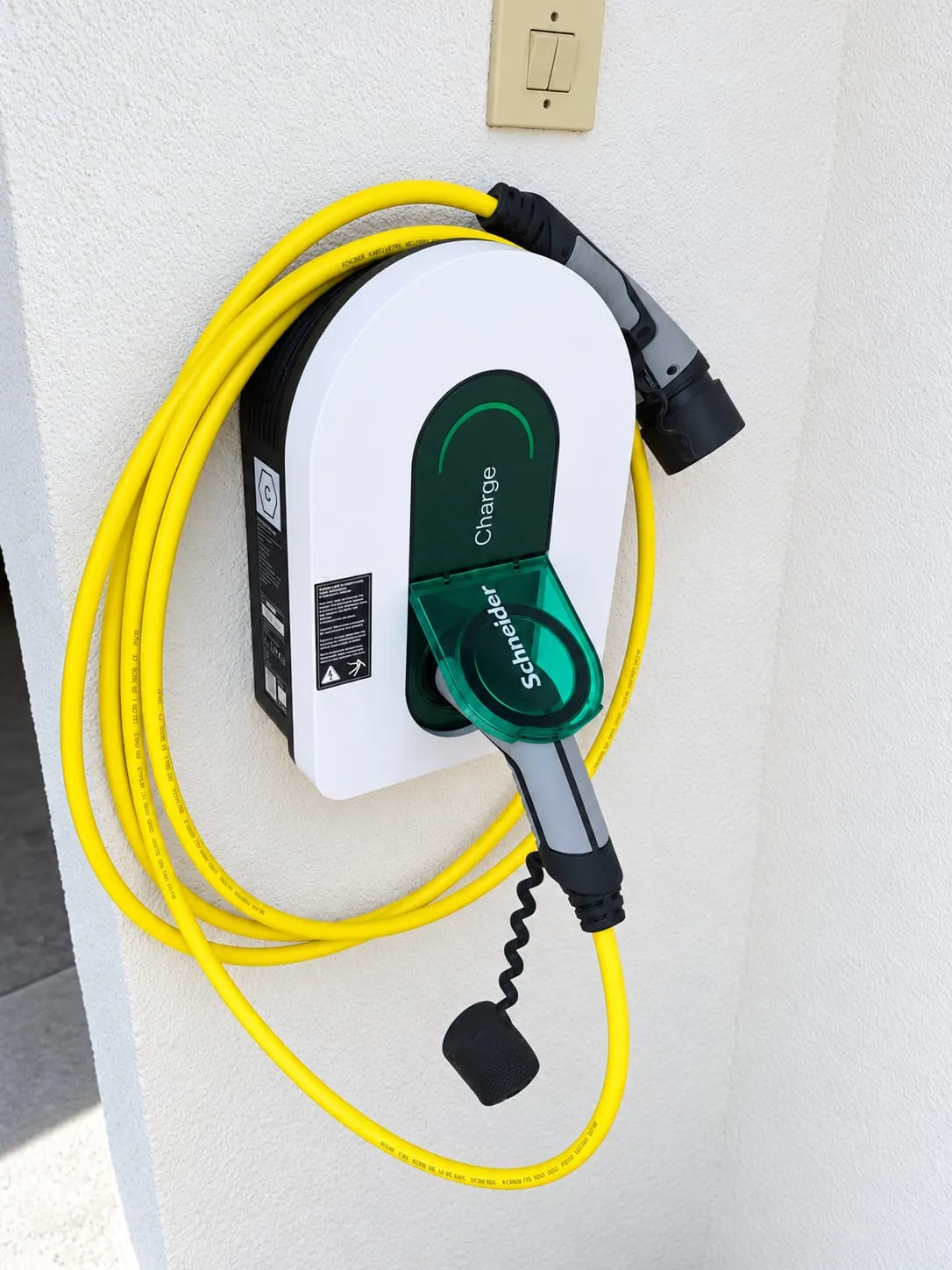 Une borne de recharge murale blanche, son câble jaune enroulé autour.