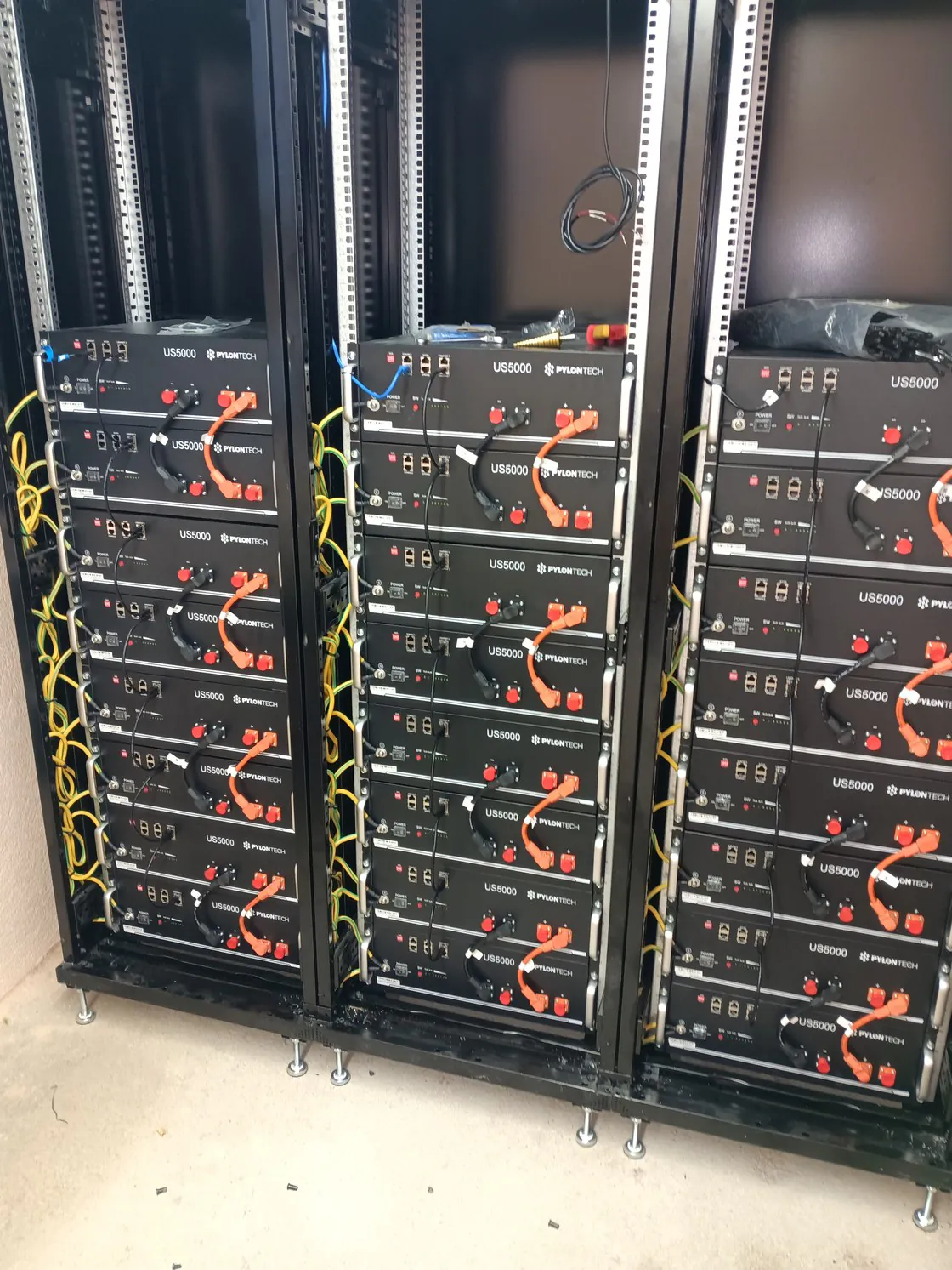 Trois baies ouvertes de batteries Pylontech reliées par des câbles orange et noirs.