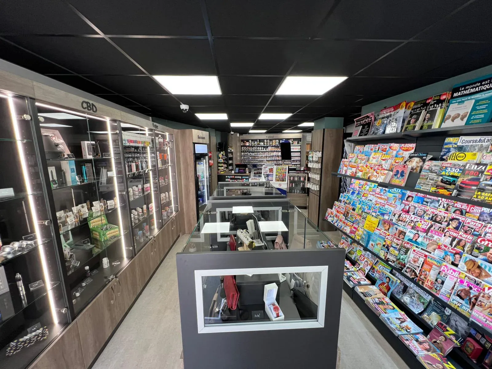 Bureau de tabac-presse agencé avec rayons magazines, vitrines fermées et comptoir de caisse face à l’entrée
