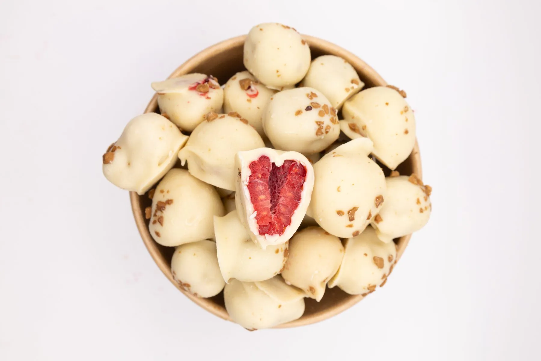 Un pot de framboises enrobées de chocolat blanc et d'éclats dorés, vu du dessus