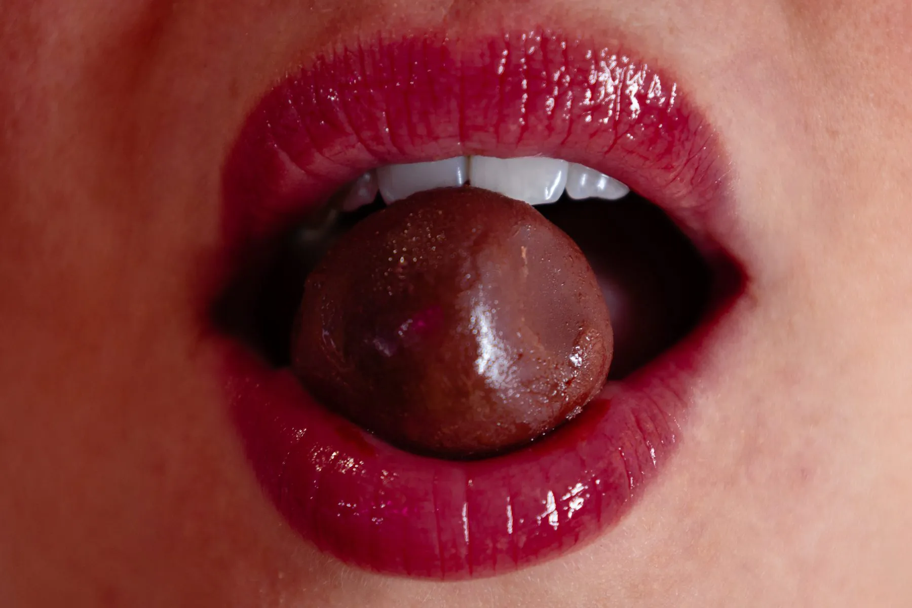 Gros plan sur une bouche croquant une framboise enrobée de chocolat