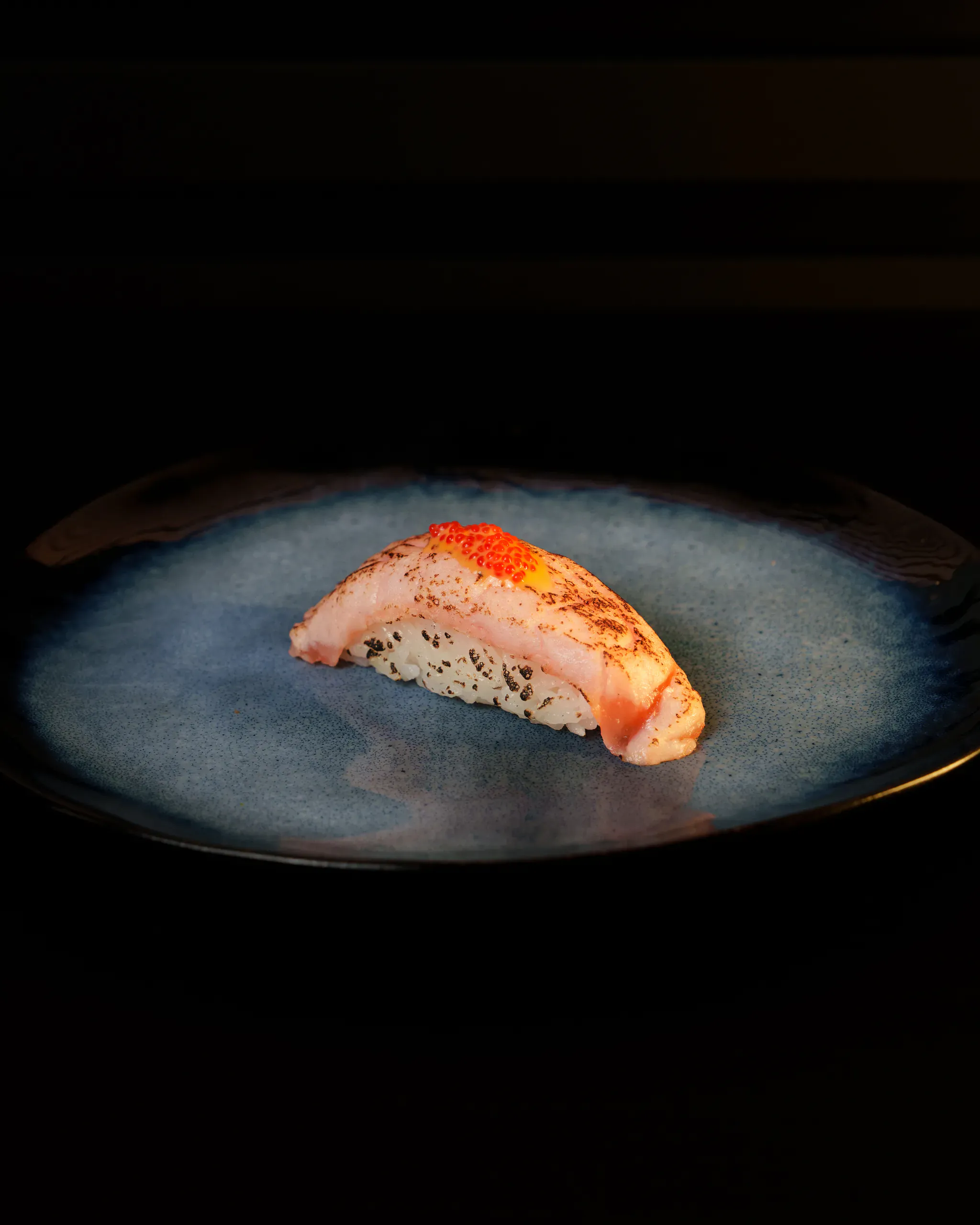 Nigiri au poisson mi-cuit flambé garni d'œufs de saumon, une pièce pensée pour une seule bouchée