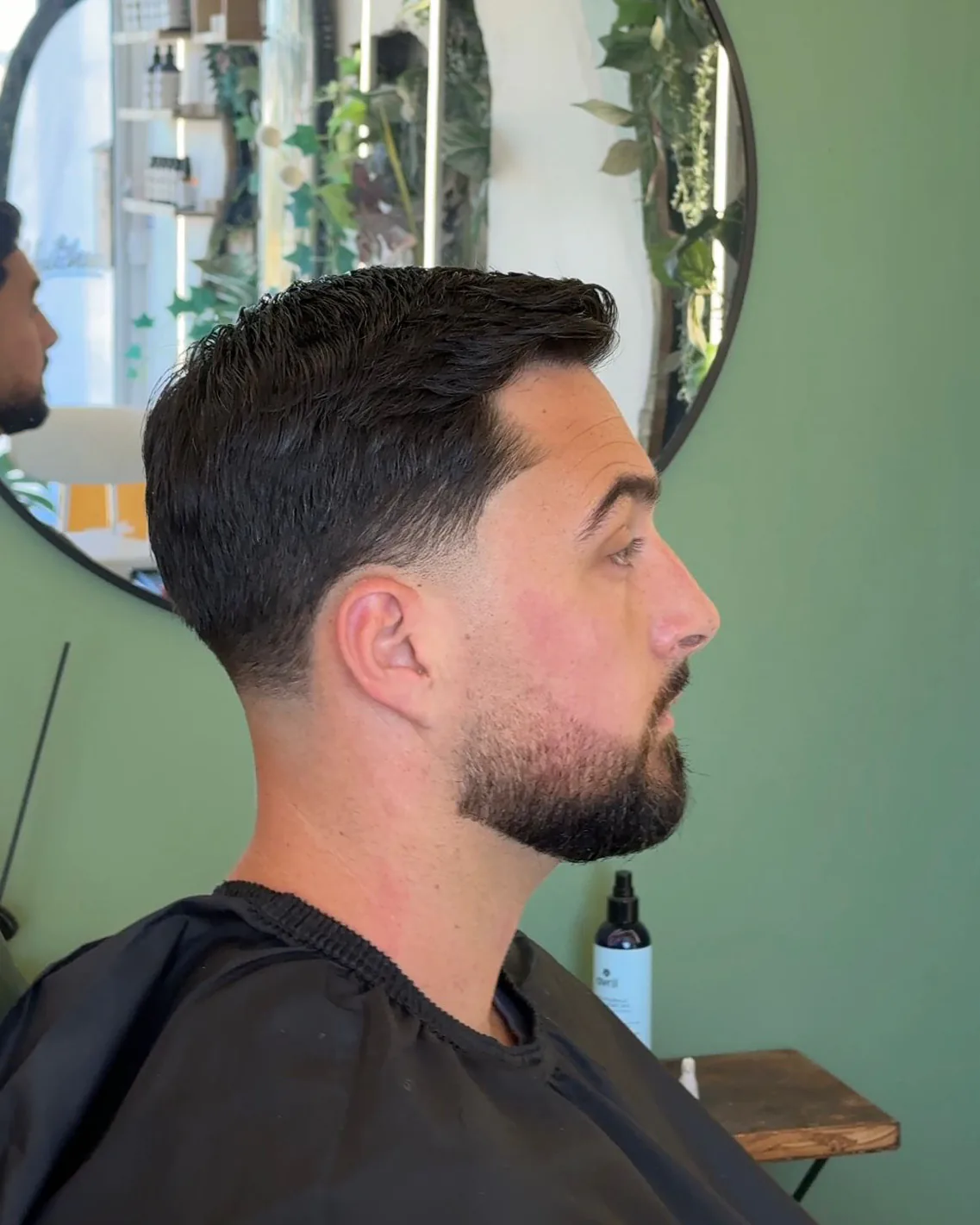 Dégradé net sur les côtés, dessus coiffé en arrière, barbe taillée
