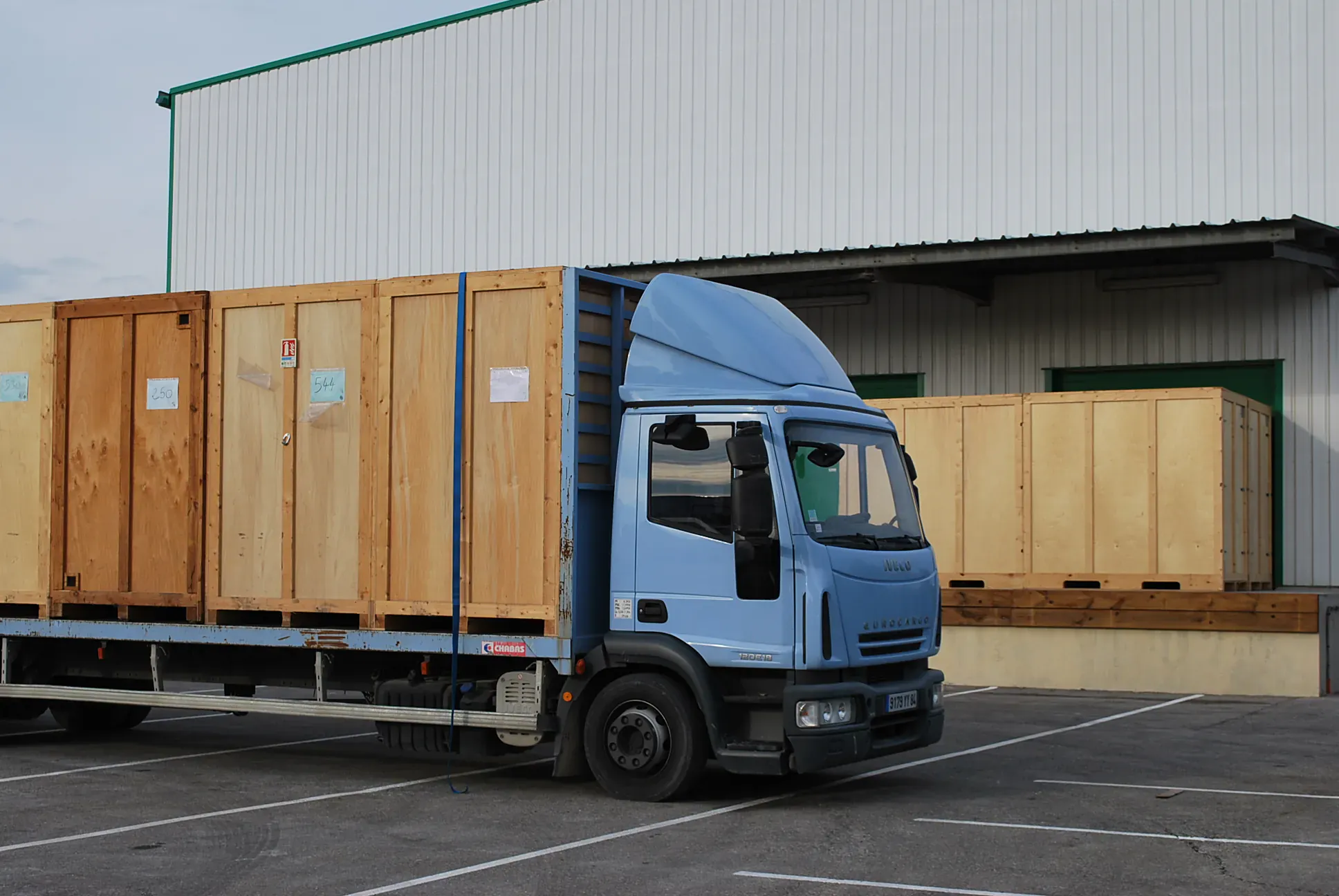 Camion Millot chargé de caisses en bois devant un entrepôt de garde-meuble