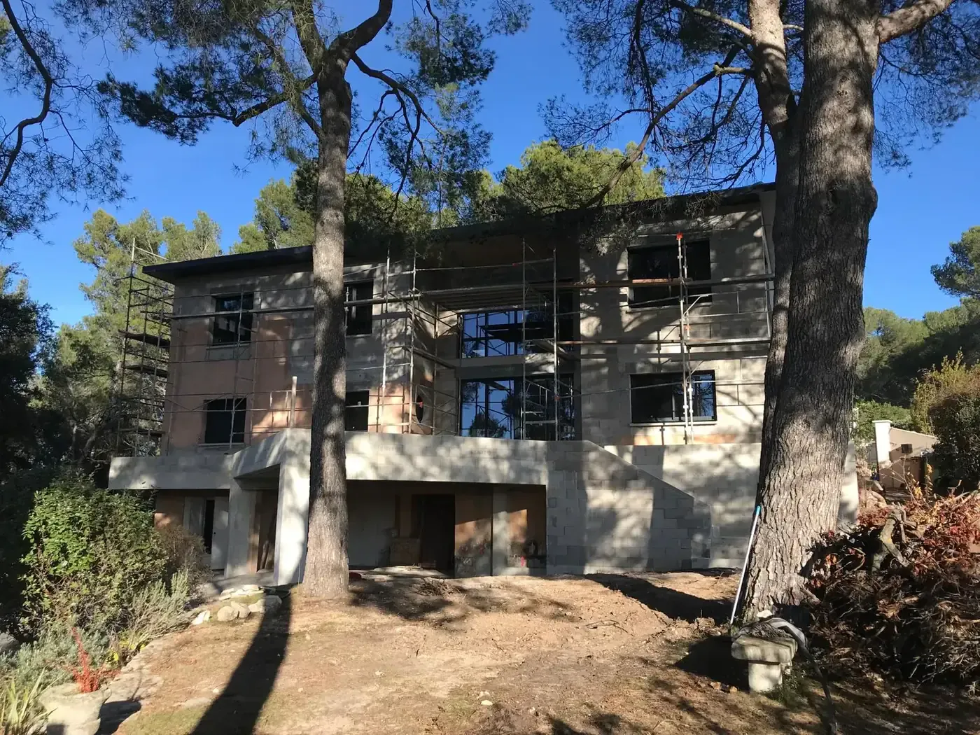 Maison individuelle moderne en cours de construction avec échafaudages, entourée de pins près de Carpentras