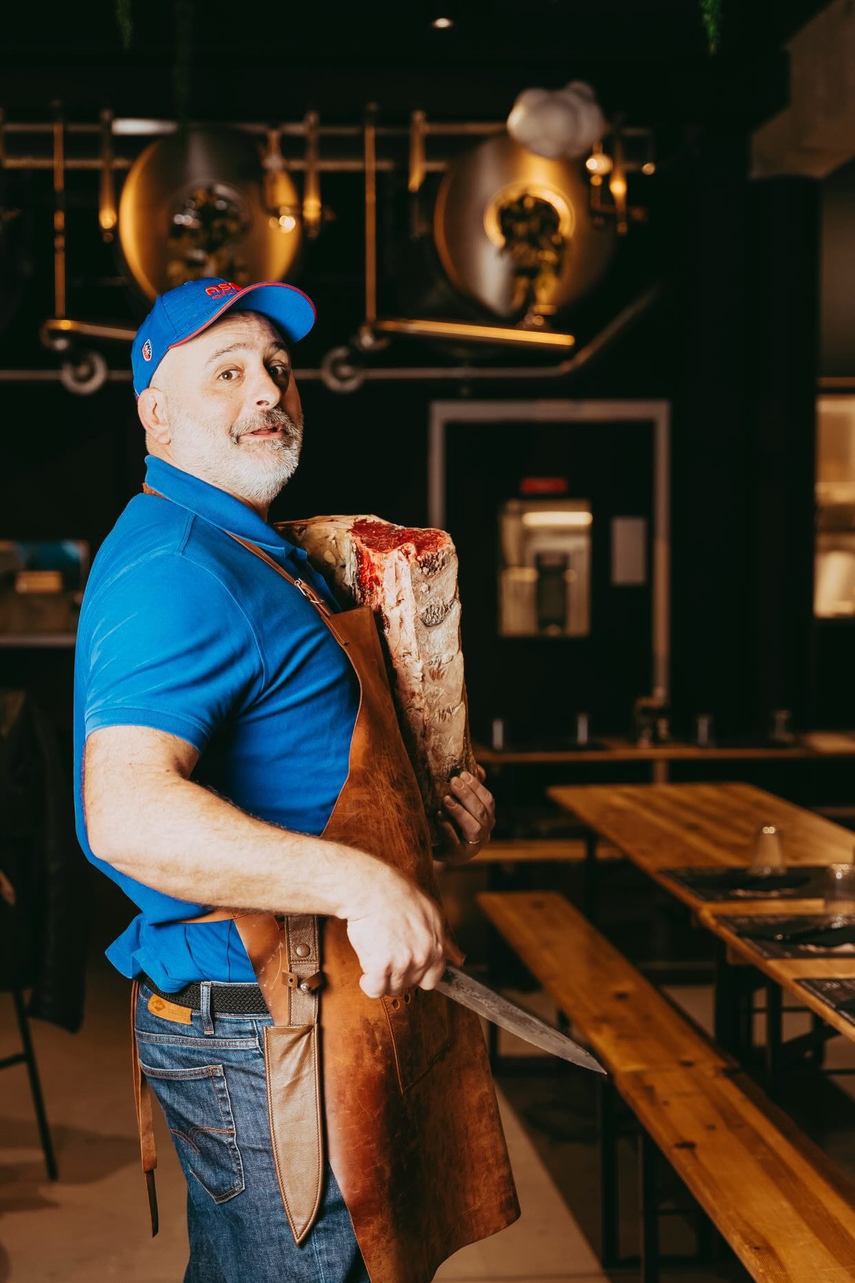Boucher en tablier de cuir tenant un couteau et une pièce de viande maturée à La Plancha des Halles, Béziers