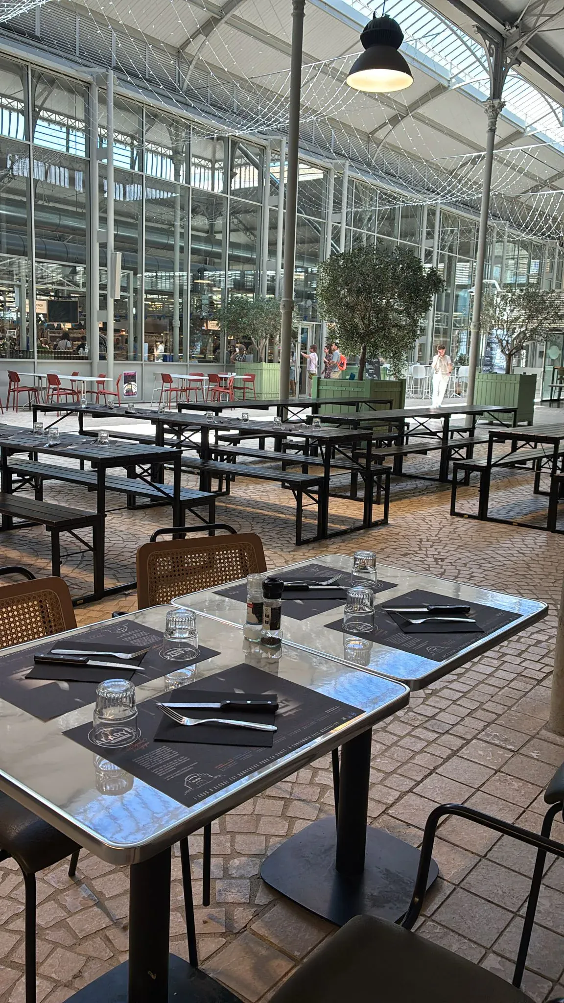Vue terrasse extérieure sous la halle, oliviers et longues tablées en bois