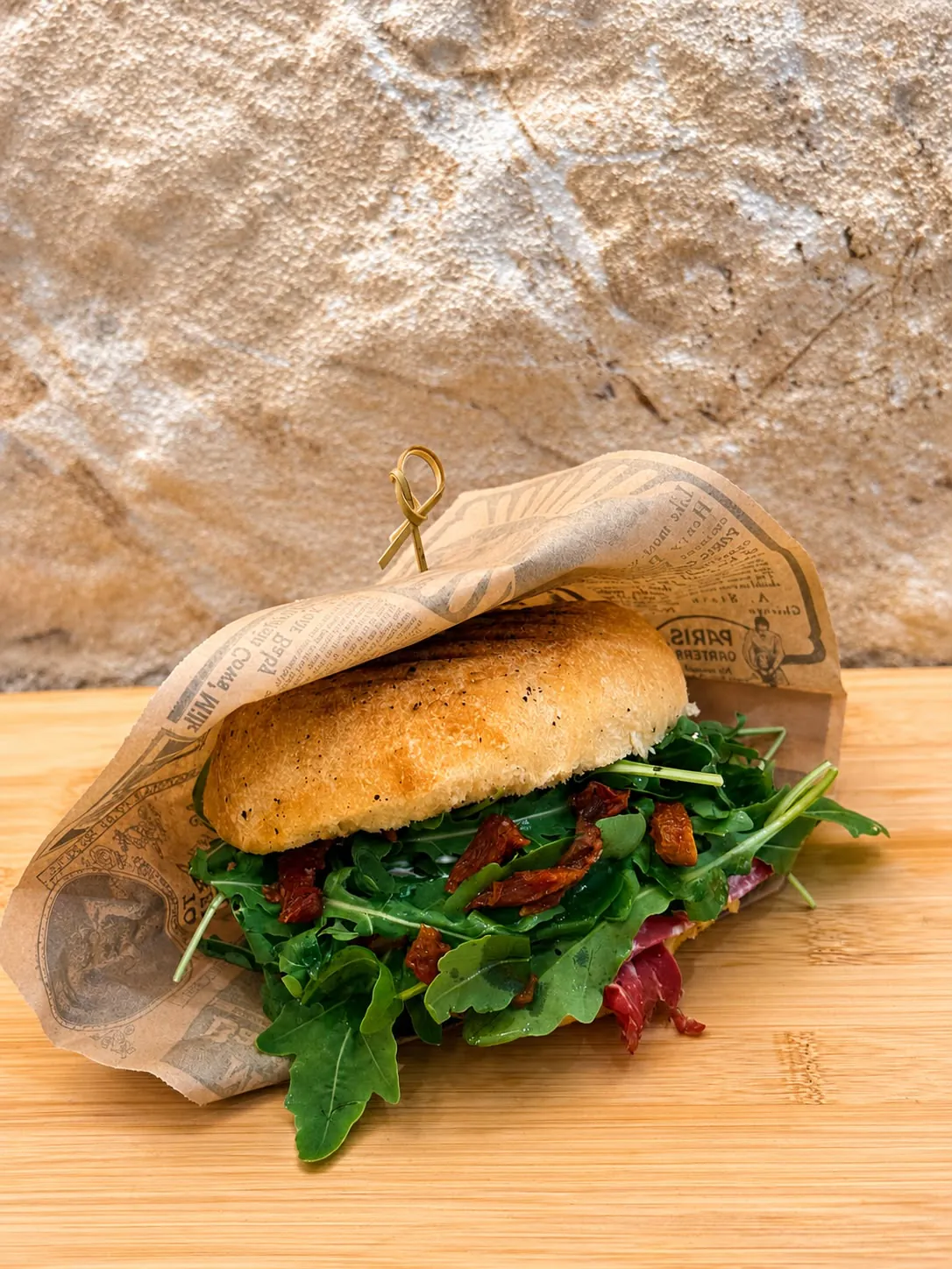 Sandwich artisanal à la roquette et aux tomates séchées, emballé dans un papier kraft