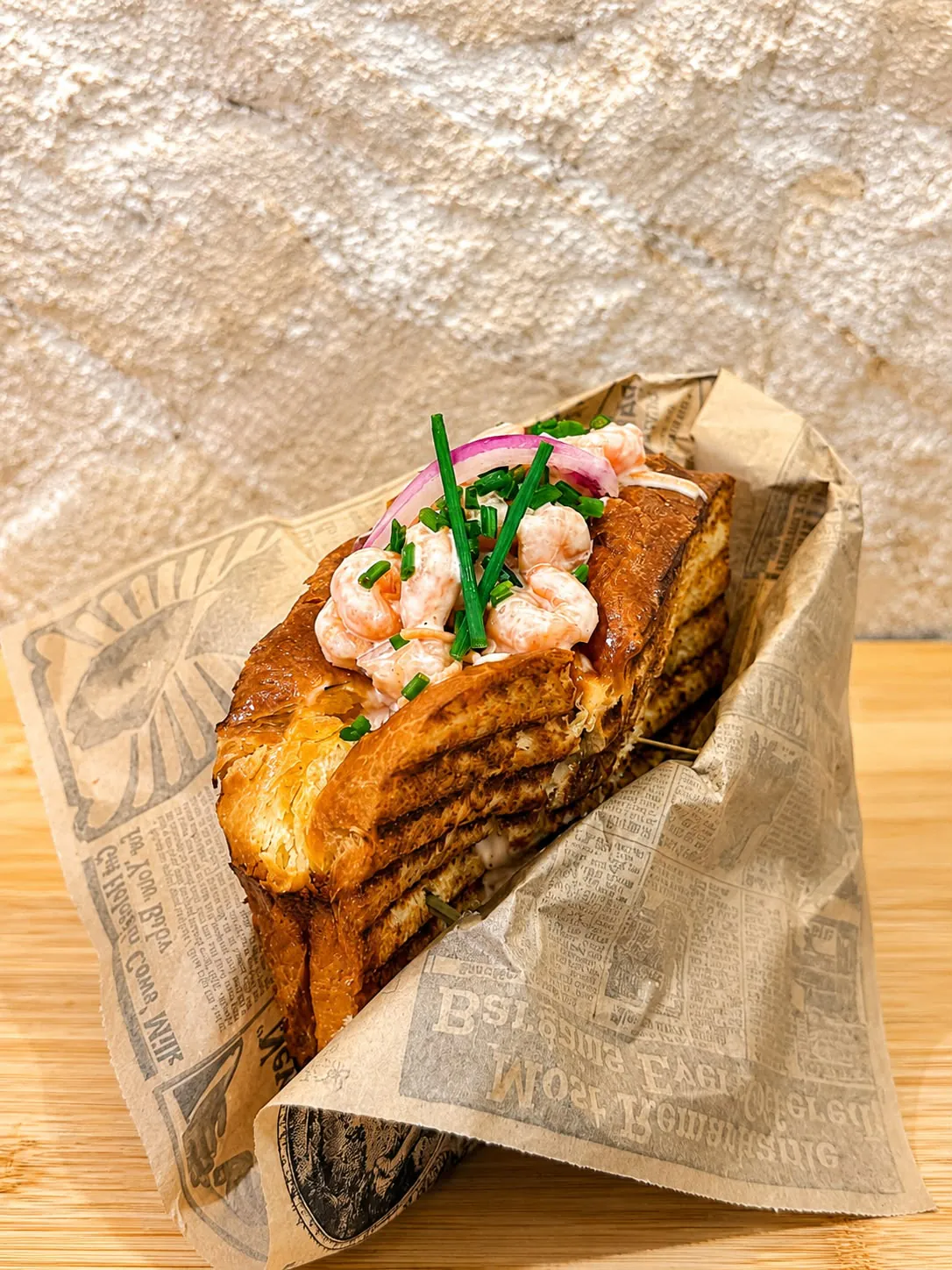 Sandwich toasté aux crevettes, ciboulette et oignon rouge, présenté dans un papier