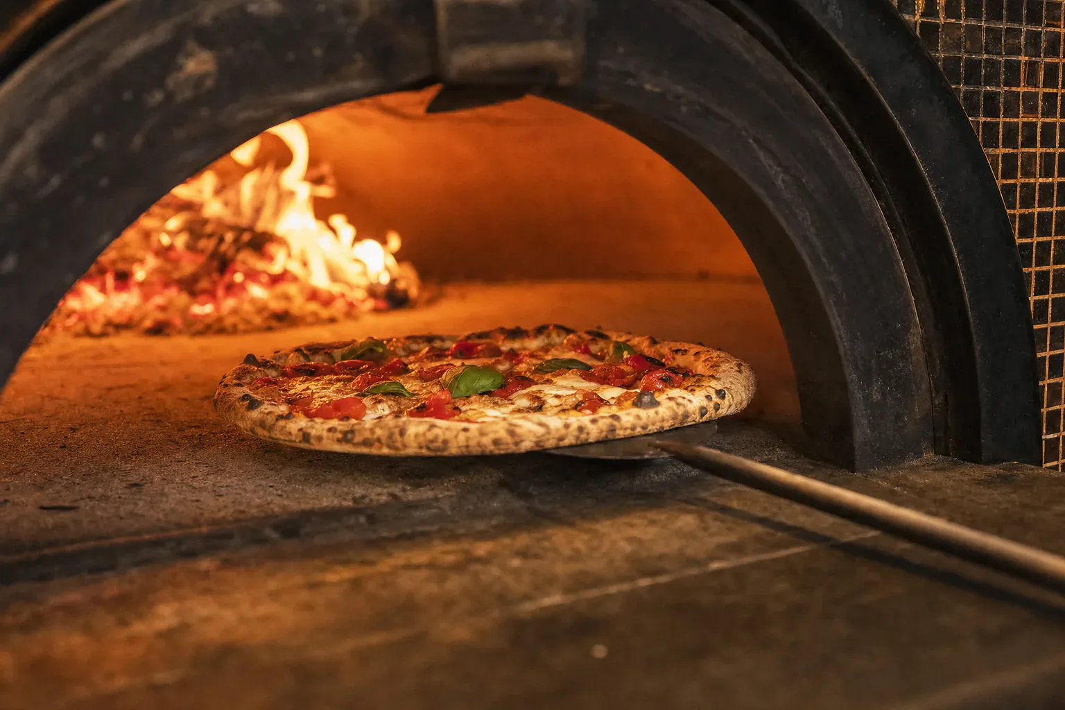 Pizza au feu de bois en pleine cuisson, bord soufflé et flammes du four Vecchio Forno au Port-Marly