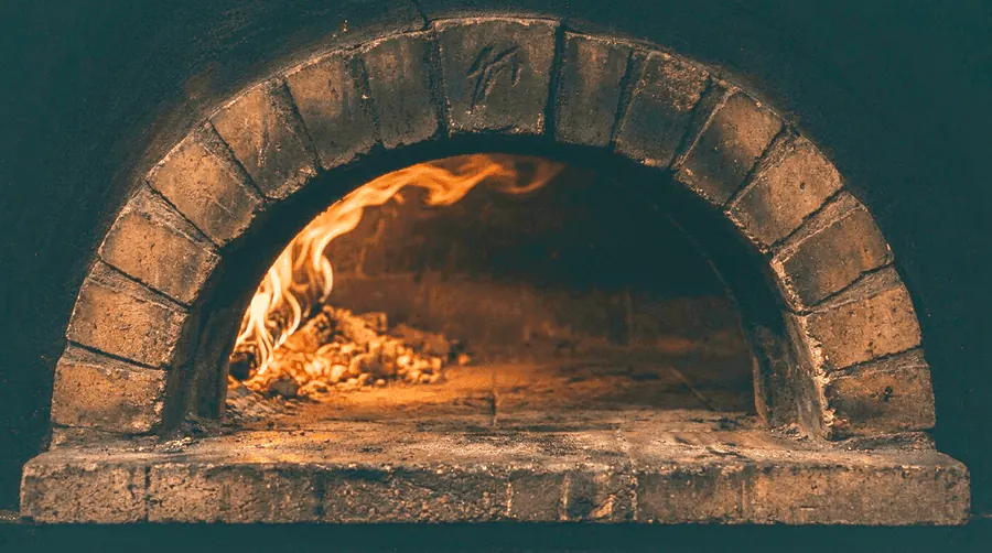 La bouche du four à bois Vecchio Forno : arc de brique, flammes et braises
