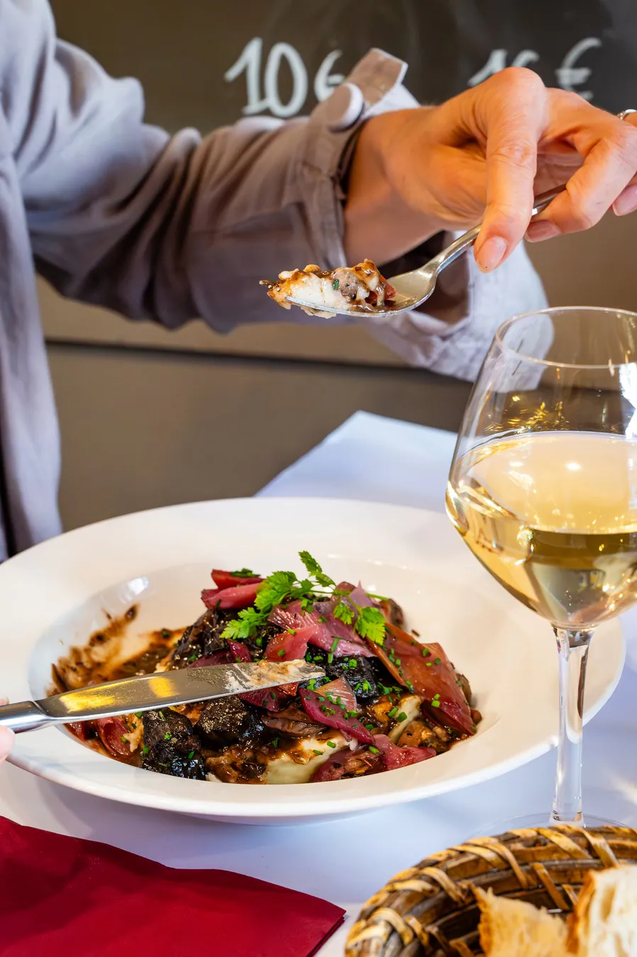 Hands cutting the beef cheek, a glass of white beside it
