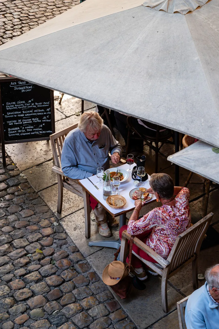 Seen from above, a couple at a terrace table on the cobbles