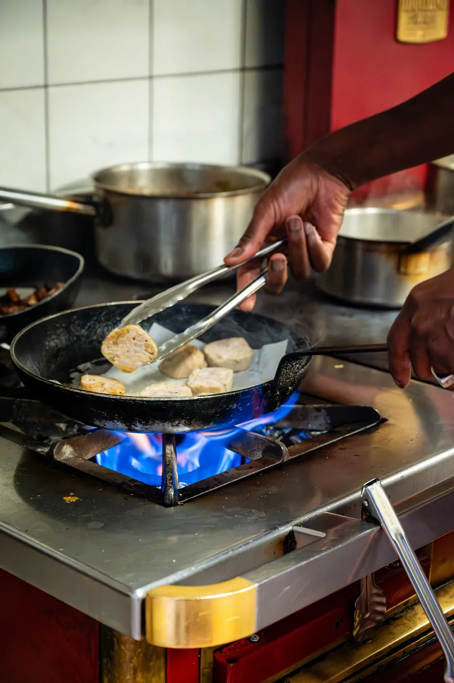 A hand turning golden pieces in the pan with tongs