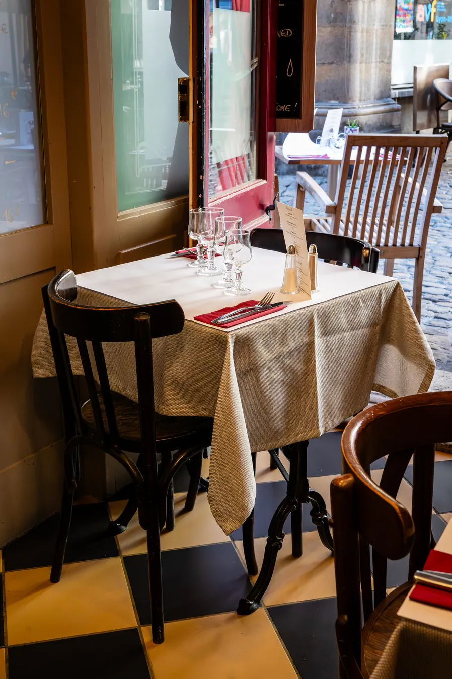A white-linen table on the chequered floor, by the window