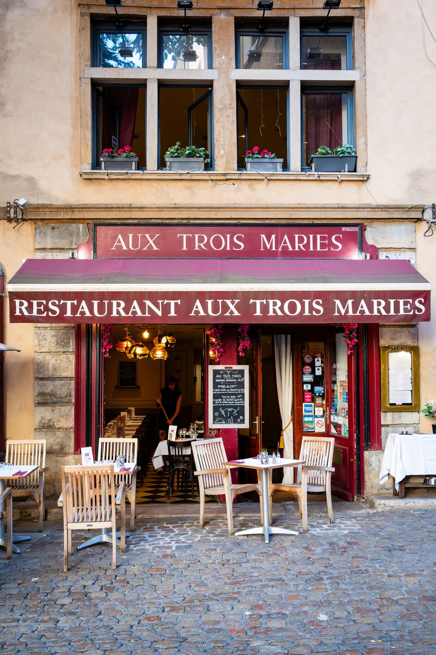 The golden-stone façade and its flowered windows, above the sign