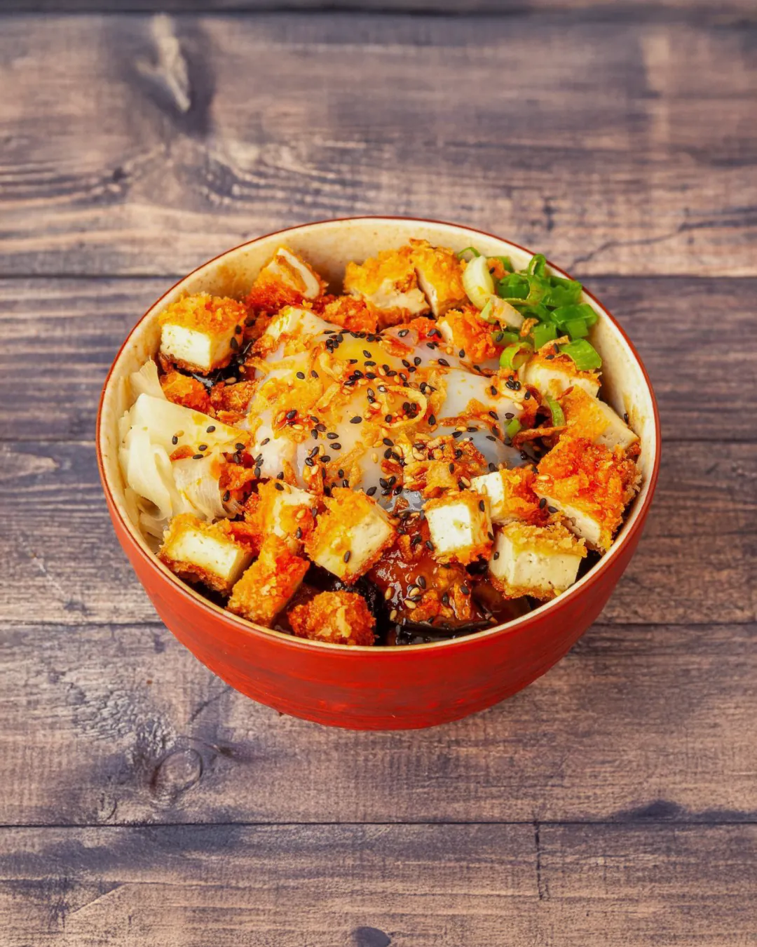 Donburi de riz au tofu frit, aubergine confite et œuf parfait dans un bol rouge laqué