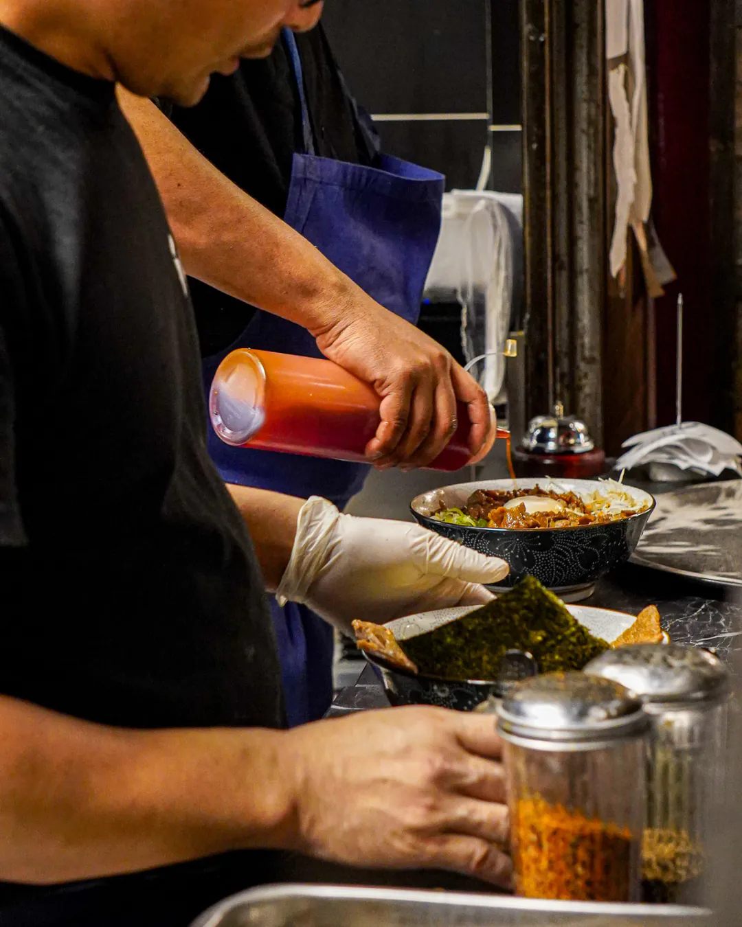 Cuisinier versant le taré sur un donburi au pass de la cuisine d'Iwao