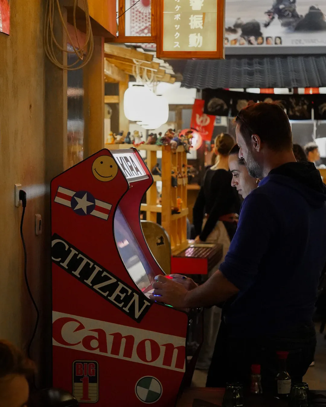 Deux clients jouant à la borne d'arcade d'Iwao