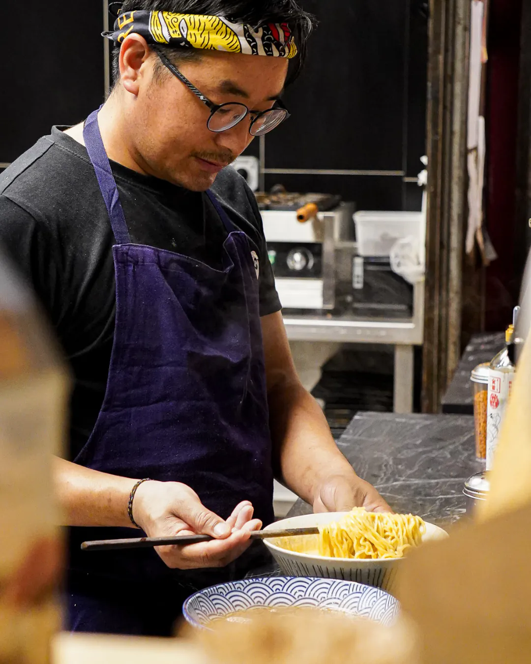 Cuisinier d'Iwao égouttant des nouilles ramen dans la cuisine ouverte
