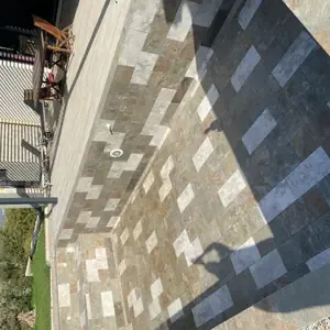 Terrasse en pavés de pierre naturelle vue en plongée, avec emplacements de jardinières et de massifs le long de la maison