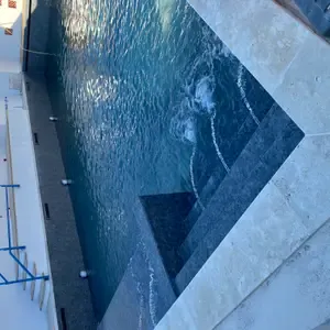 Piscine à débordement en béton armé en cours de construction, bordée de pierre et d'un escalier immergé