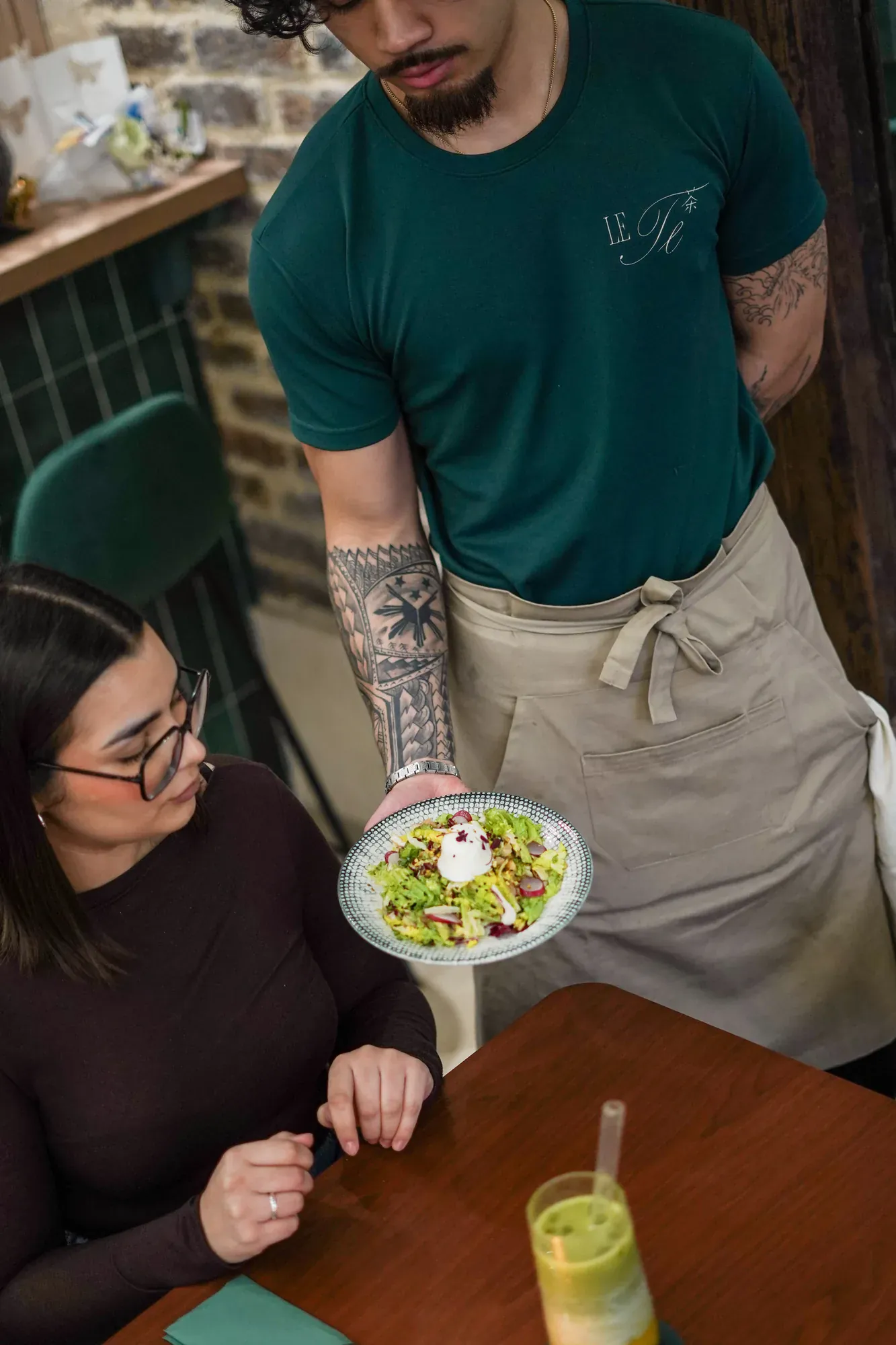 Serveur Le Te tatoue sert salade a cliente, t-shirt vert logo