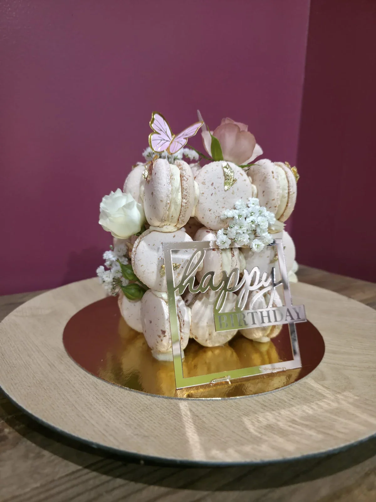 Gâteau d'anniversaire recouvert de macarons roses et décoré de fleurs fraîches