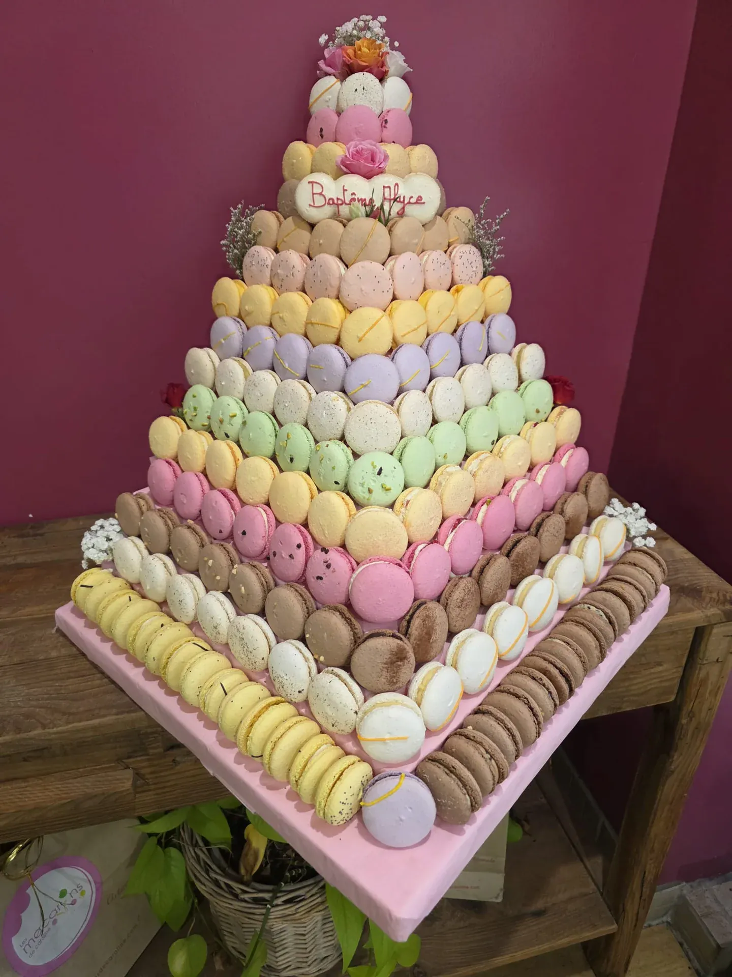 Pièce montée pyramidale 10 étages en macarons, gradient pastel doux du rose au chocolat, fleurs fraîches au sommet et plaque personnalisée, création événementielle artisanale