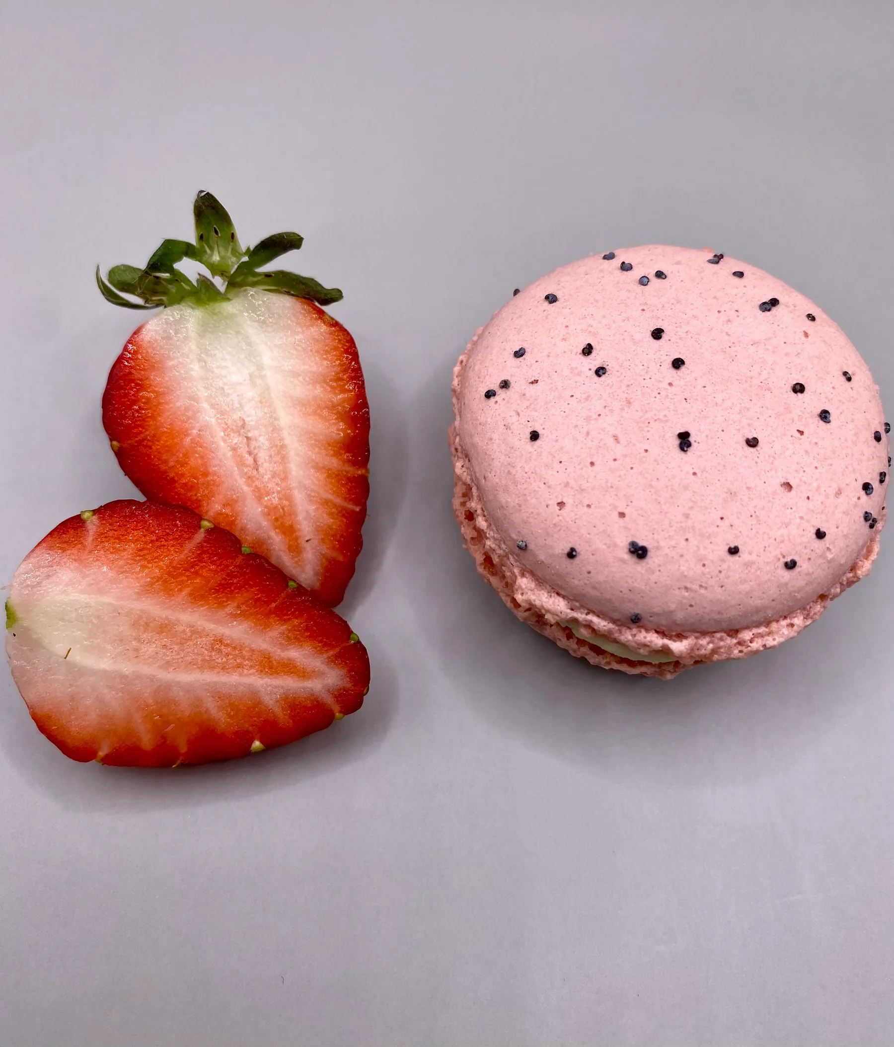 Macaron rose moucheté posé près d'une fraise coupée, garniture aux fruits frais dans l'esprit provençal