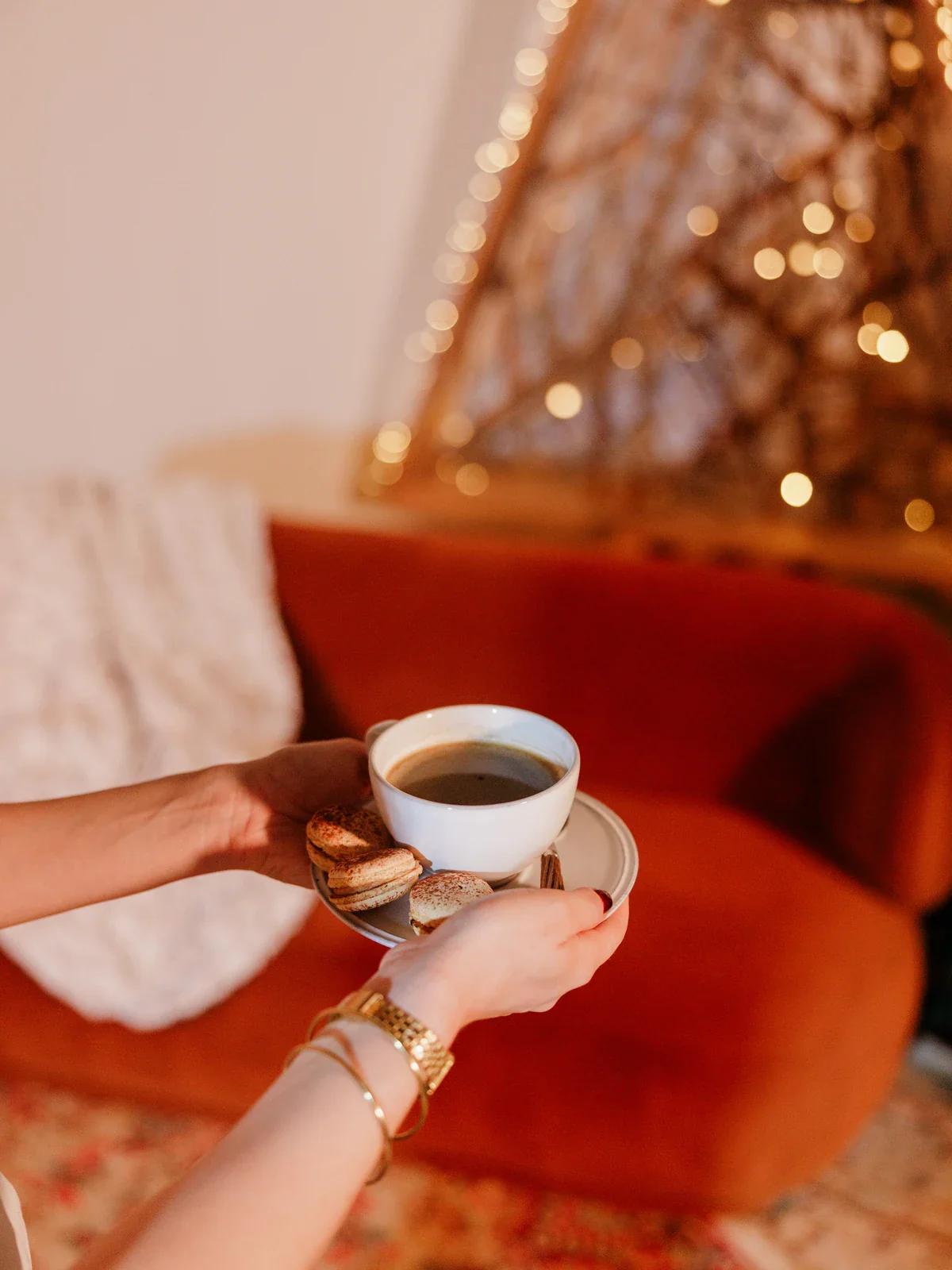 Des mains tiennent une tasse de café accompagnée de macarons, moment de partage convivial
