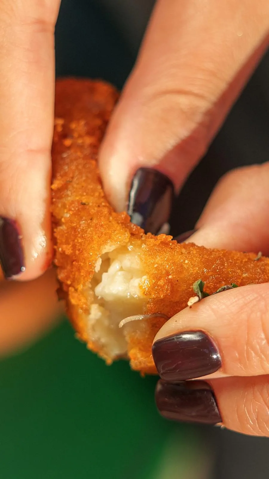 Deux mains cassent en deux une croquette panée dorée faite maison, révélant le fromage fondu