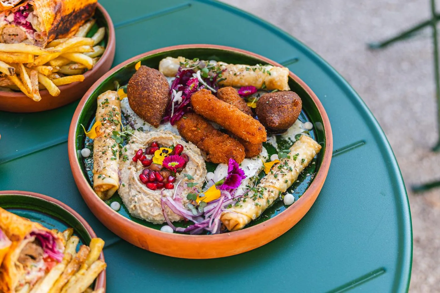 Houmous crémeux garni de grenade et d'herbes, entouré de falafels