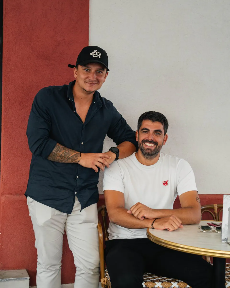 Deux hommes de l’équipe du Petit Rouet, souriants, devant la faïence rouge de la terrasse