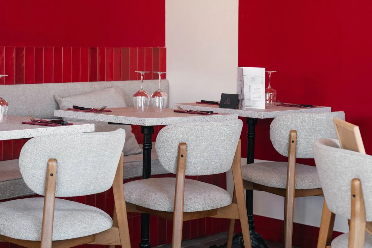 La salle sous l’arche de faïence rouge : tables dressées, verres à pied et chaises claires