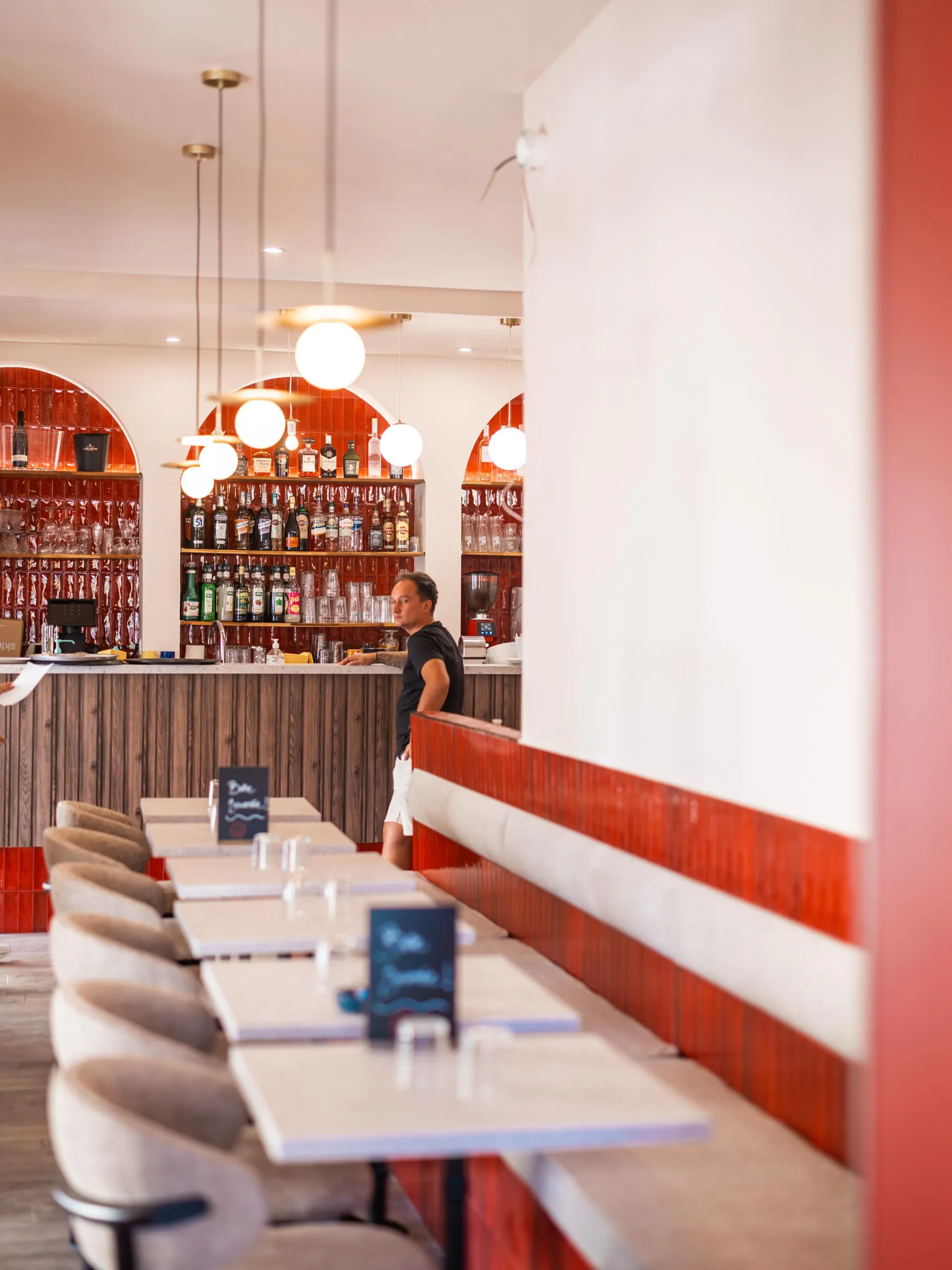 Le comptoir sous les arches de faïence rouge, la banquette et les tables dressées