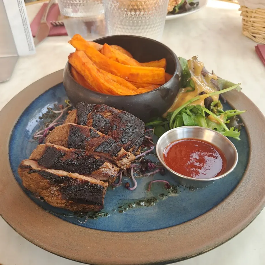 Une viande grillée, des frites de patate douce et une salade dans une assiette