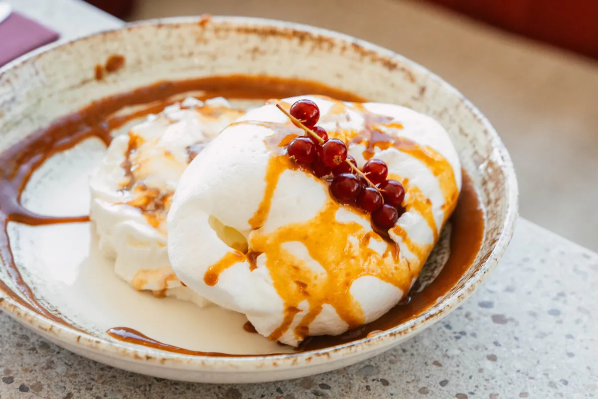 Un dessert crémeux nappé de caramel et de groseilles, dans une assiette creuse
