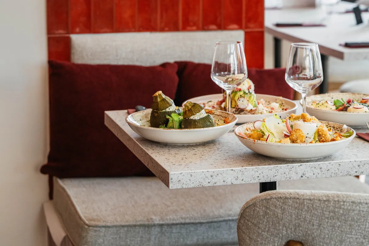 Une table servie le long de la banquette, des assiettes et des verres de vin, devant la faïence rouge