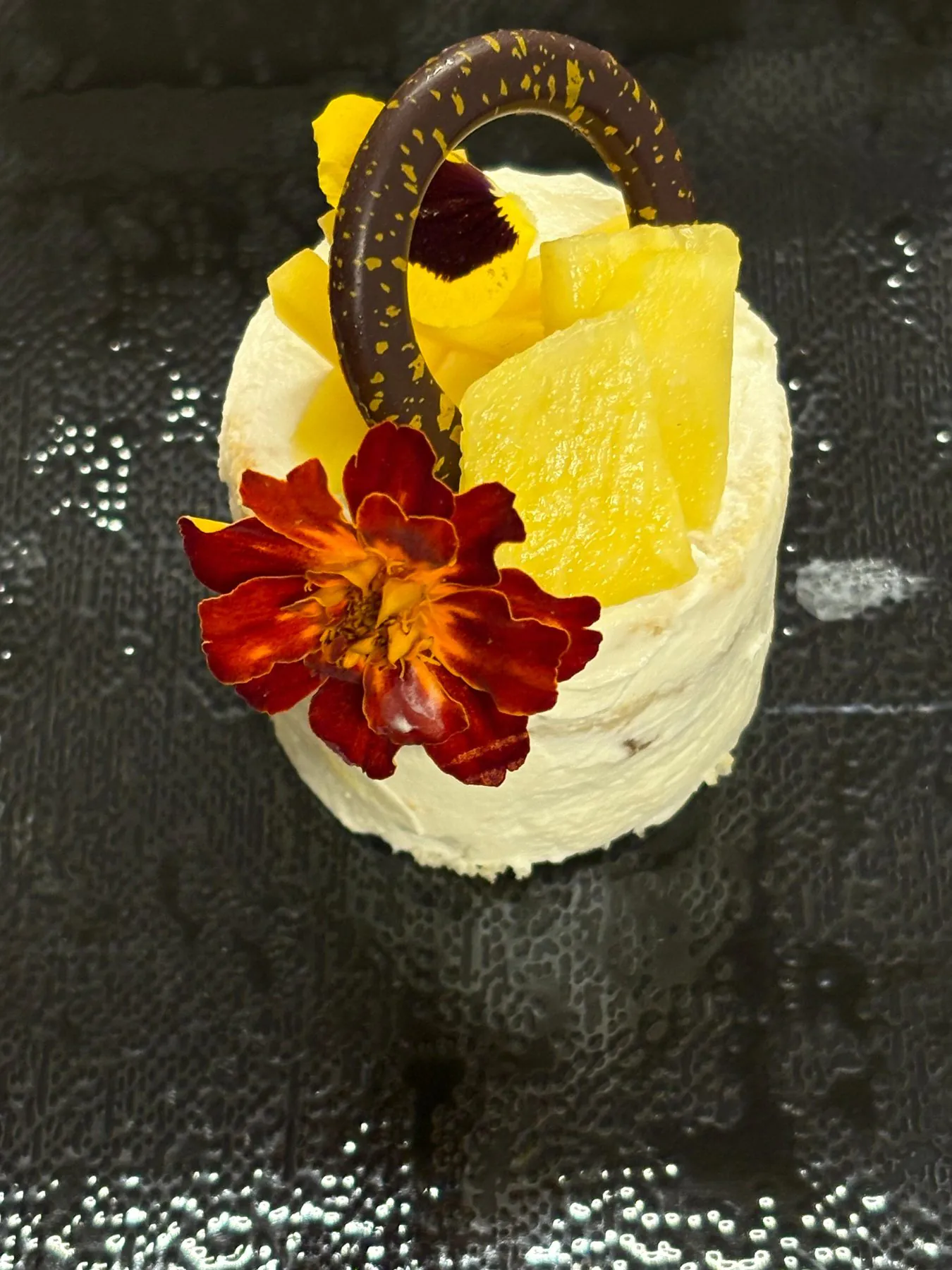 Entremets individuel crémeux garni d’ananas, d’un anneau en chocolat et de fleurs comestibles