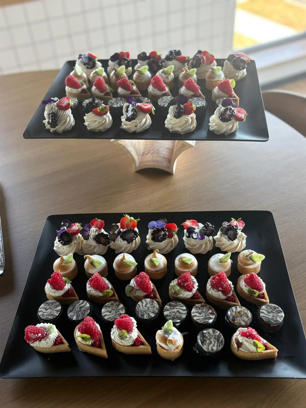 Deux plateaux noirs en étagère de mignardises : pavlovas aux fruits rouges et tartelettes