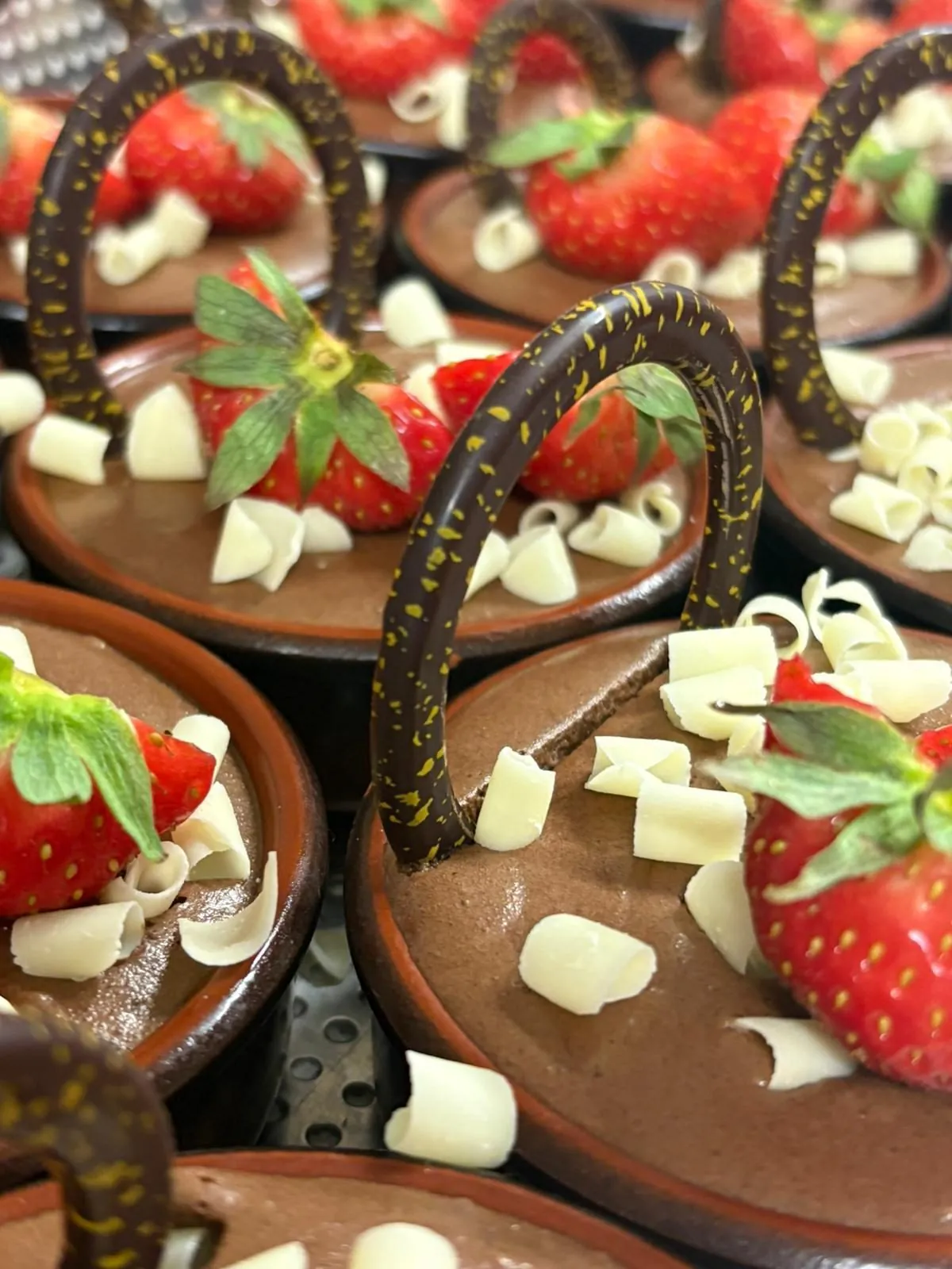Mousses au chocolat servies en petits pots de terre cuite, décorées de fraises