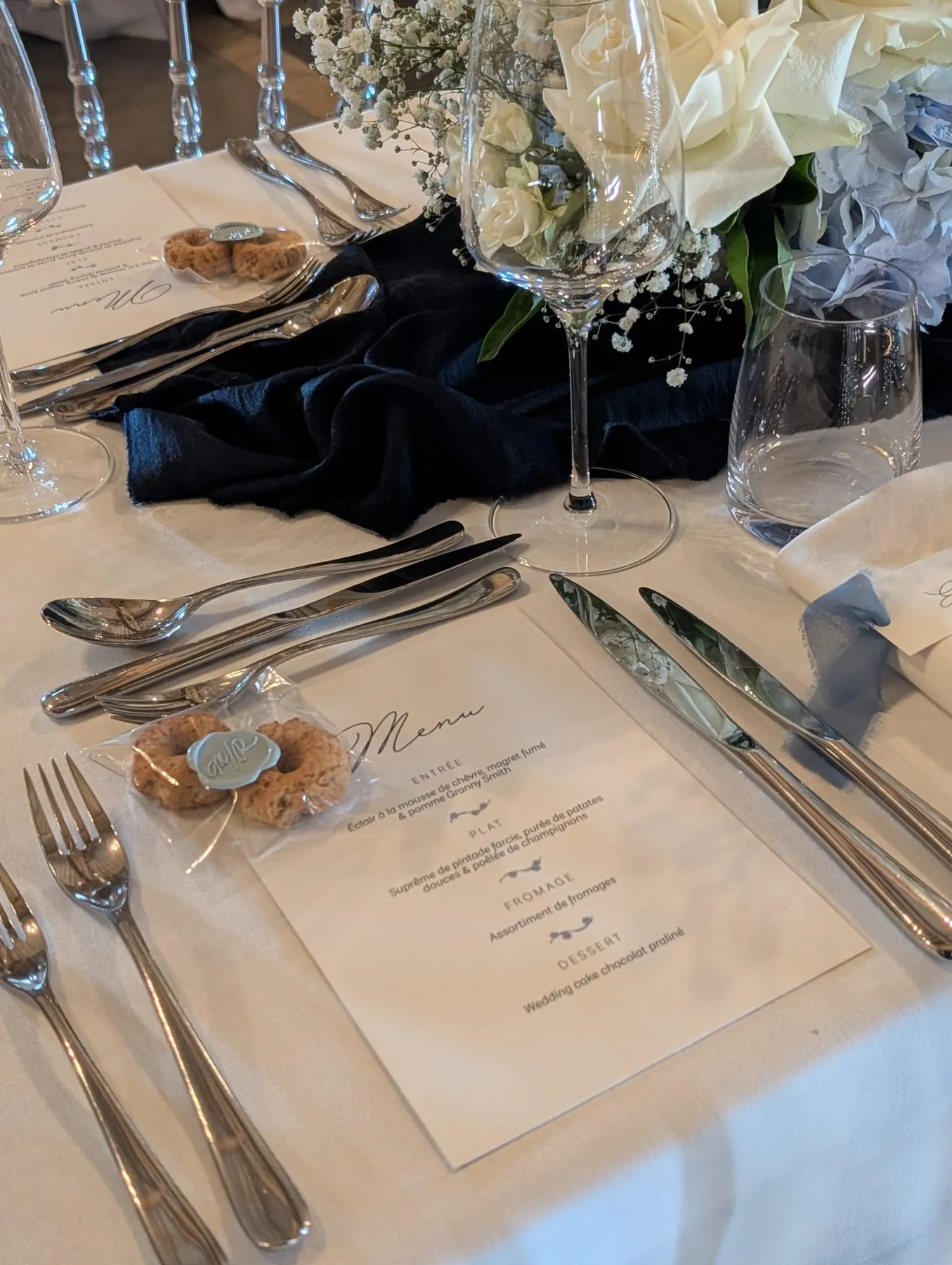Table de mariage dressée avec menu imprimé, couverts argentés, chemin de table et décoration florale