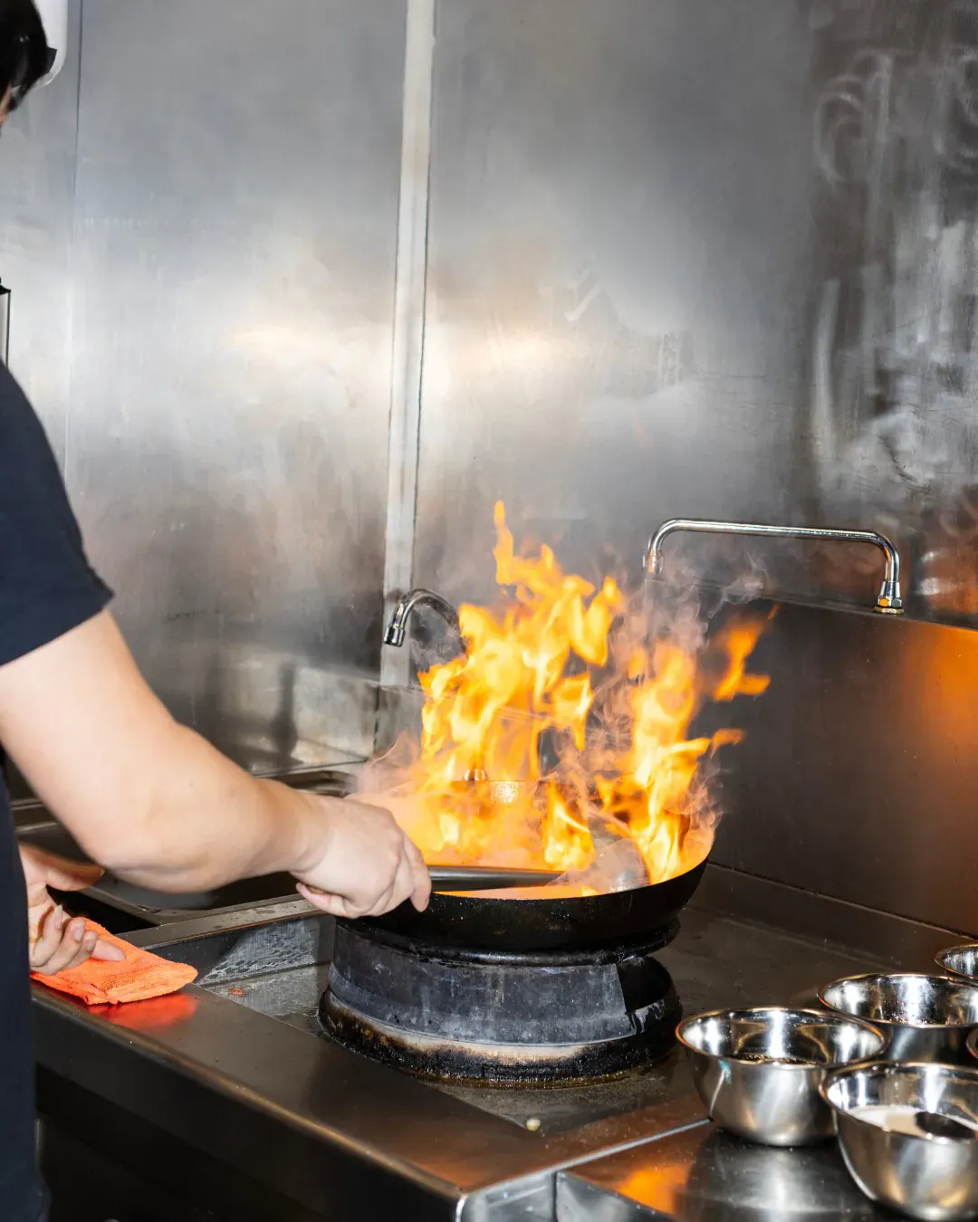 Wok en action dans la cuisine de Phở 98, flamme montante au-dessus du feu vif