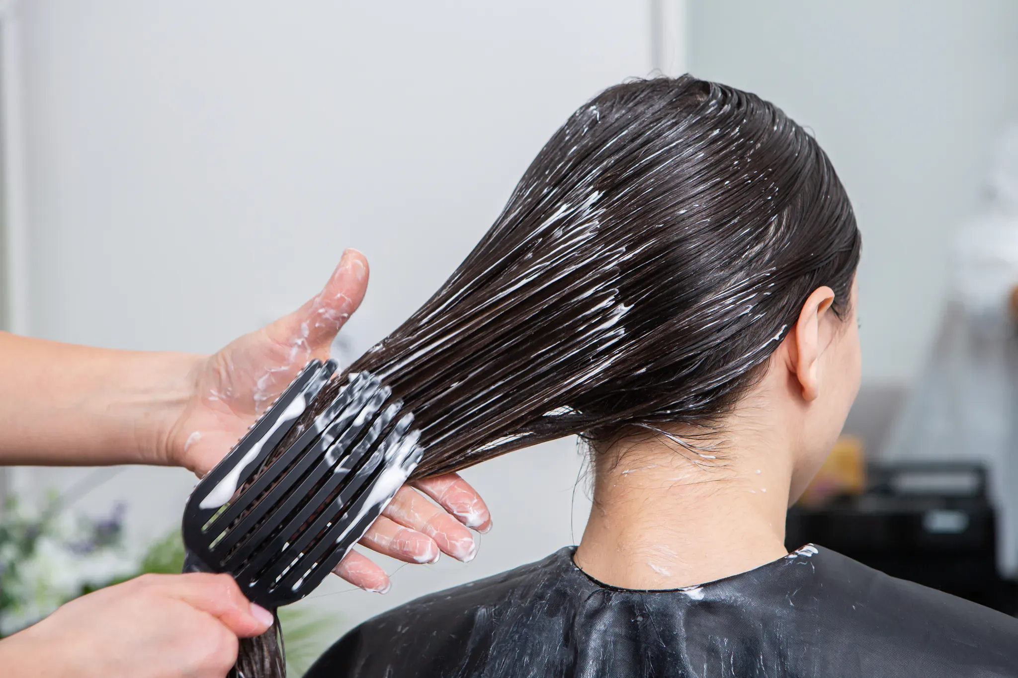 Application d'un soin capillaire au peigne avant la pose d'extensions au salon d'Étampes