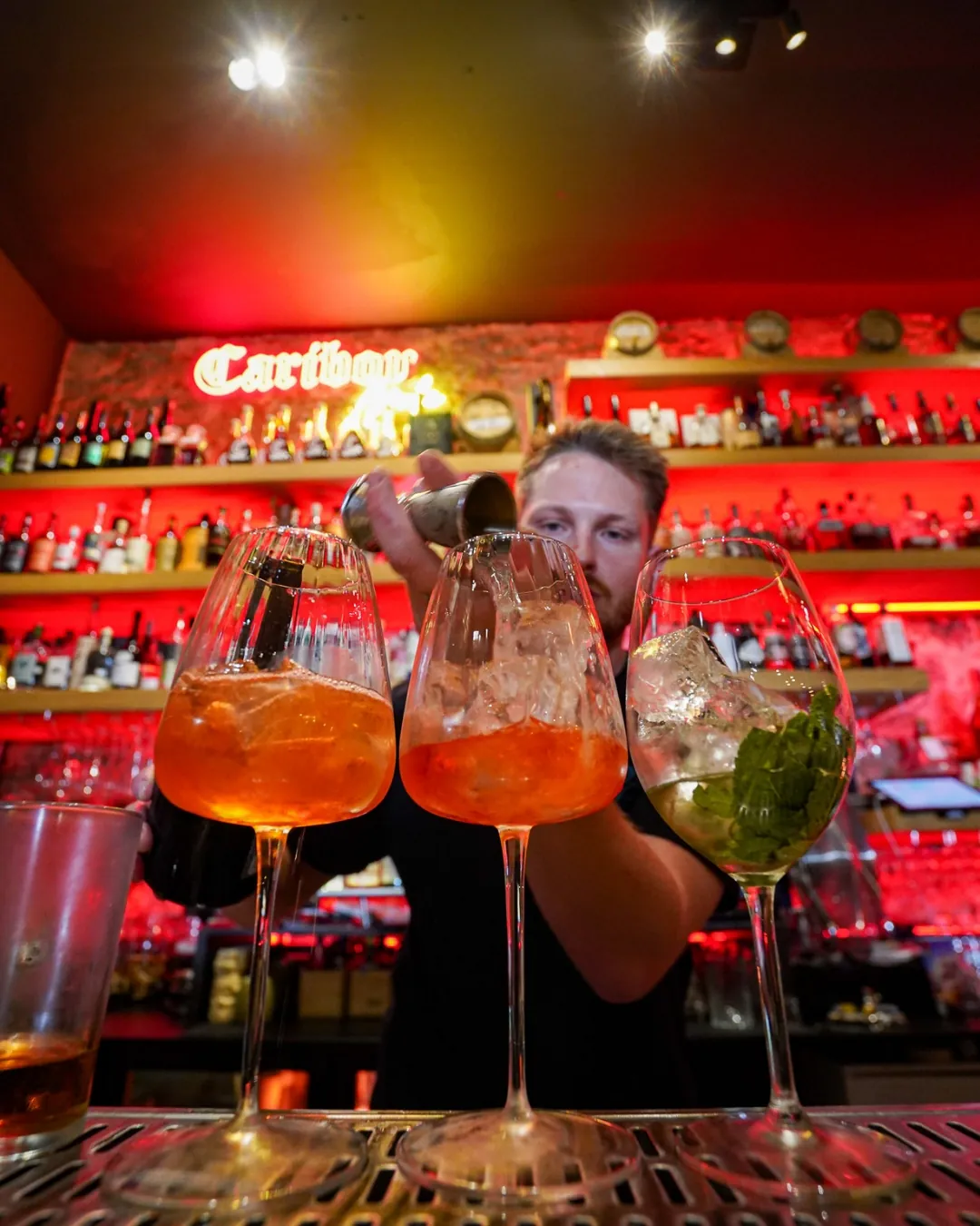 Barman du Caribou versant des cocktails devant le back-bar et l'enseigne néon